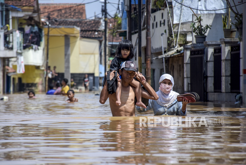 Warga menggendong anaknya melintasi genangan air saat banjir (ilustrasi)