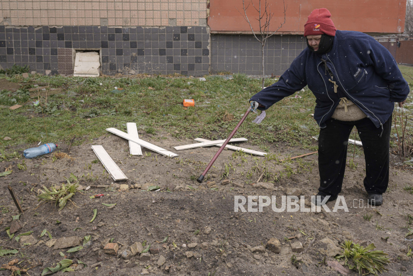 Seorang wanita menunjuk ke kuburan darurat seorang pria yang dibunuh oleh pasukan Rusia, menurut penduduk, dan dikuburkan di luar gedung apartemen karena orang-orang tidak dapat membawanya ke pemakaman di Bucha, Ukraina, Ahad, 3 April 2022.