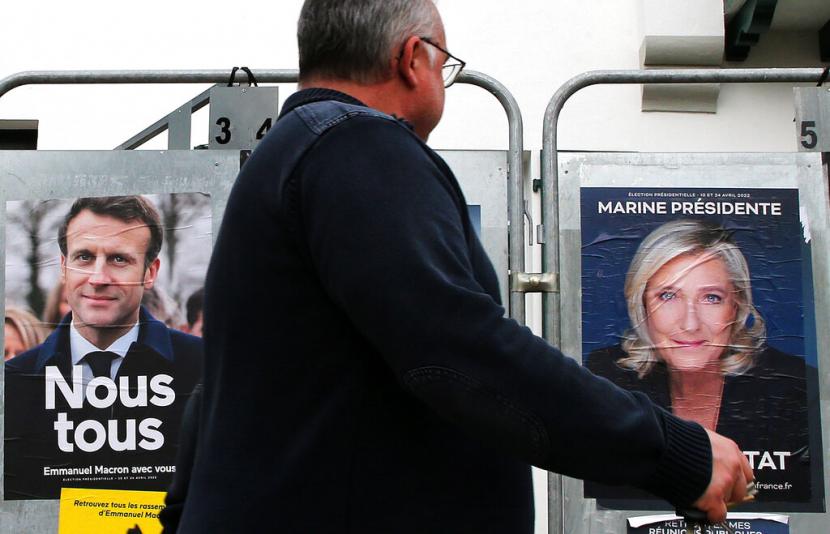 Seorang pria berjalan melewati poster kampanye presiden dari Presiden Prancis dan kandidat tengah untuk pemilihan kembali Emmanuel Macron dan kandidat presiden sayap kanan Prancis Marine Le Pen di Anglet, barat daya Prancis, Rabu, 8 April 2022.