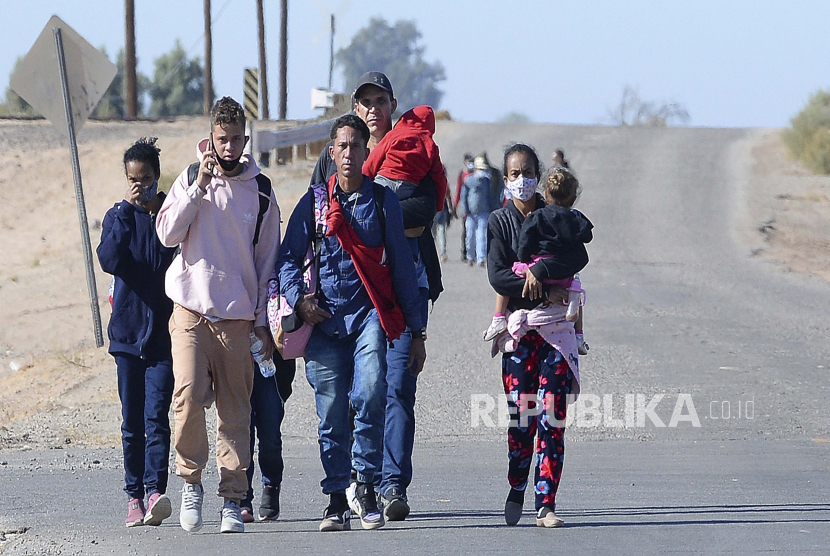 Seorang pria muda berbicara di ponsel saat ia dan sekelompok migran yang memasuki Amerika Serikat dengan menyeberangi Sungai Colorado dari Meksiko dekat County 13th Street di Lembah Yuma Arizona, berjalan ke timur di County 14th Street di Lembah Yuma Arizona Senin pagi, 12 Desember. 6, 2021.