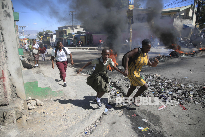 Seorang wanita dengan putrinya berjalan melewati barikade yang dipasang oleh anggota polisi di Port-au-Prince, Haiti, Kamis, 26 Januari 2023.